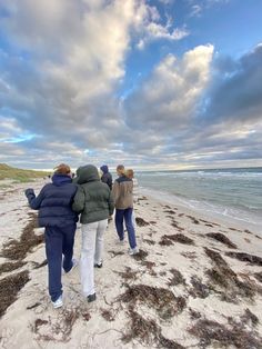 four people walking on the beach with their backs turned to the camera, under a cloudy sky