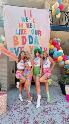 three girls are posing in front of a sign with balloons and confetti all around them