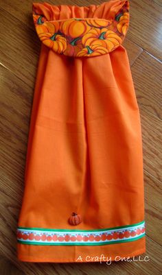 an orange dress with pumpkins on it is laying on the wooden floor next to a pair of scissors