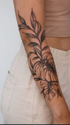 a woman's arm with a tattoo on it that has flowers and leaves on it