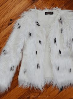 a white fur jacket with black spots on the front and back, sitting on a wooden floor