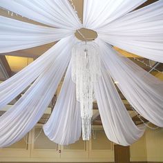 a chandelier hanging from the ceiling with white drapes and lights on it