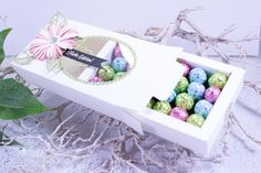 a white box filled with lots of colorful candies next to a leafy plant