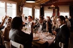 a group of people sitting around a table with wine glasses in front of them and one person raising his hand