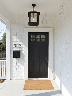 a black front door on a white house with a light hanging from the ceiling above it