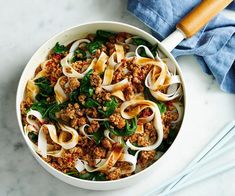 a white bowl filled with noodles and meat on top of a table next to chopsticks