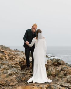 a bride and groom standing on rocks by the ocean