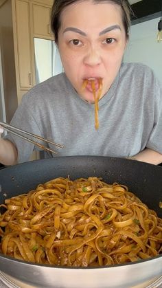 a woman eating noodles in a pan with chopsticks sticking out of her mouth