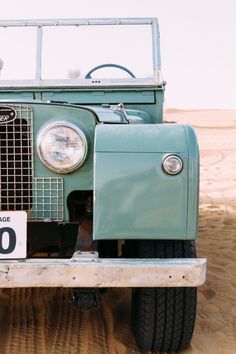 an old green truck is parked in the sand and has a number plate on it