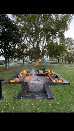 a fire pit in the middle of a grassy area with candles lit on it and trees