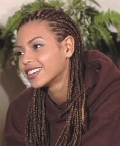 a woman with long braids sitting in front of a potted plant and smiling