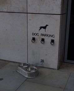 a dog parking sign on the side of a building next to a metal bowl with water in it