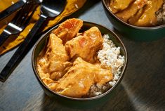 two bowls filled with curry and rice on top of a wooden table next to utensils