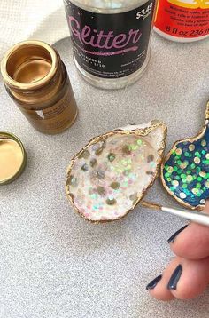 a person holding a paintbrush next to some confetti tins and other crafting supplies