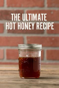 the ultimate hot honey recipe in a mason jar on a wooden table next to a brick wall