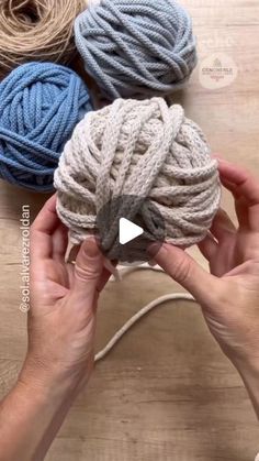 two hands holding balls of yarn on top of a wooden table