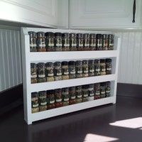 a shelf filled with lots of spices on top of a black floor next to a white wall