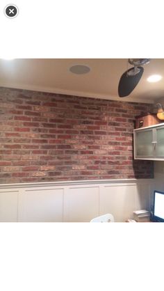 a brick wall in an office with a computer on the desk and a fan hanging from the ceiling