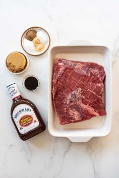 raw meat in a white dish next to condiments and seasonings on a marble counter top