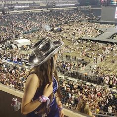 a woman wearing a cowboy hat standing in front of an arena full of people at a concert