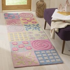 a colorful rug is on the floor next to a purple chair and vase with flowers