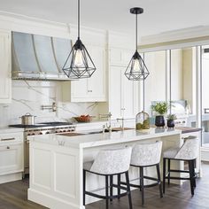 a kitchen with white cabinets and marble counter tops, an island with stools is shown