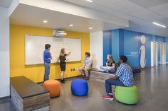 three people are sitting in front of a whiteboard while another person is writing on it