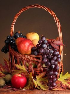 a basket filled with lots of fruit sitting on top of a wooden table next to leaves