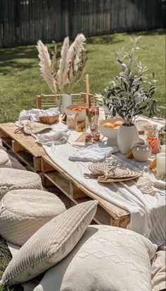 an outdoor table set up with pillows, plates and vases on top of it