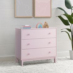 a pink dresser with two pictures on the wall and a potted plant next to it