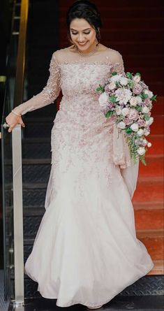 a woman in a wedding dress is walking down the stairs with her bouquet on her hand