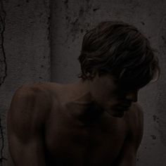 a shirtless man with no shirt standing in front of a wall and looking at his cell phone