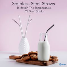 a bottle of milk next to some cookies on a wooden board with straws in it