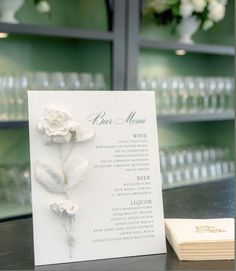 a menu with white flowers on it sitting next to a glass case filled with liquor