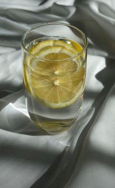 a glass filled with water sitting on top of a white cloth covered tablecloth next to a slice of lemon