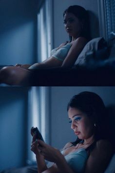 a woman sitting in bed looking at her cell phone while holding the remote control up to her chest