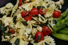 pasta with spinach, tomatoes and green beans on a black plate next to peas