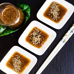 three small white plates topped with food next to chopsticks and a glass filled with liquid