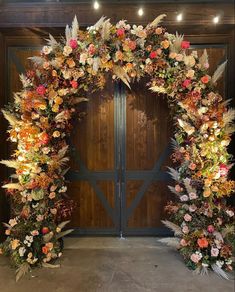 an outdoor wedding arch decorated with flowers and foliage for the entrance to the reception hall