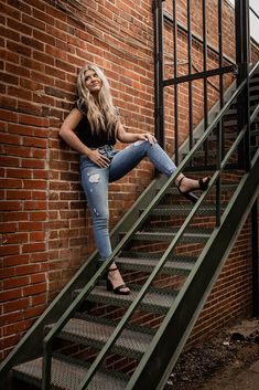 a woman sitting on top of a set of stairs next to a brick wall and metal railing