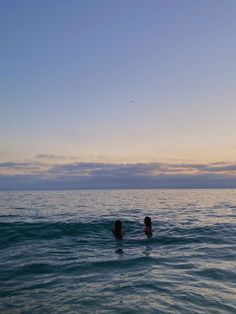 two people are swimming in the ocean at sunset or dawn, one is holding his head back