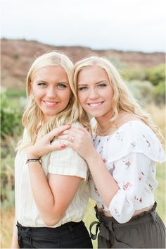 two beautiful young women standing next to each other in front of a desert landscape with grass and bushes