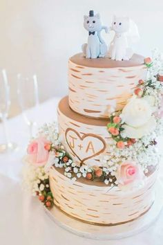 a wedding cake with two cats on top and flowers in the middle, sitting on a table