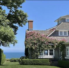 a house with flowers growing on the side of it and water in the back ground