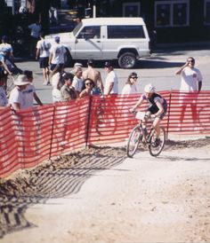 a man riding a bike down a dirt road next to a red and white fence