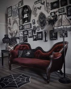 a red couch sitting in front of a wall covered with pictures and framed photos on it