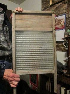 an old man holding up a wooden frame with metal slats on the bottom and sides