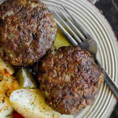 two hamburger patties with pickles and potatoes on a plate next to a fork