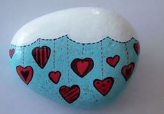 a painted rock with hearts hanging from it's sides on a white surface and blue background