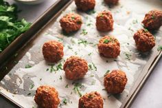 meatballs on a baking sheet with parsley and seasoning next to them, ready to be cooked